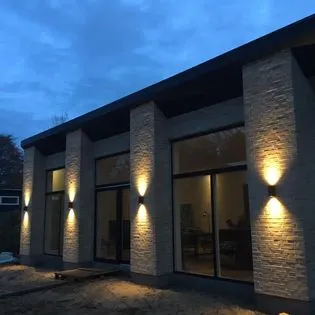 Nybygget hus med murede søjler og udendørsbelysning i skumringen